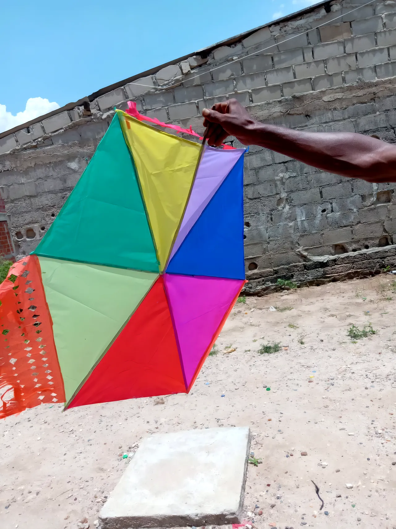 Un barrilete hexagonal de papel de colores, sostenido en alto contra el cielo
