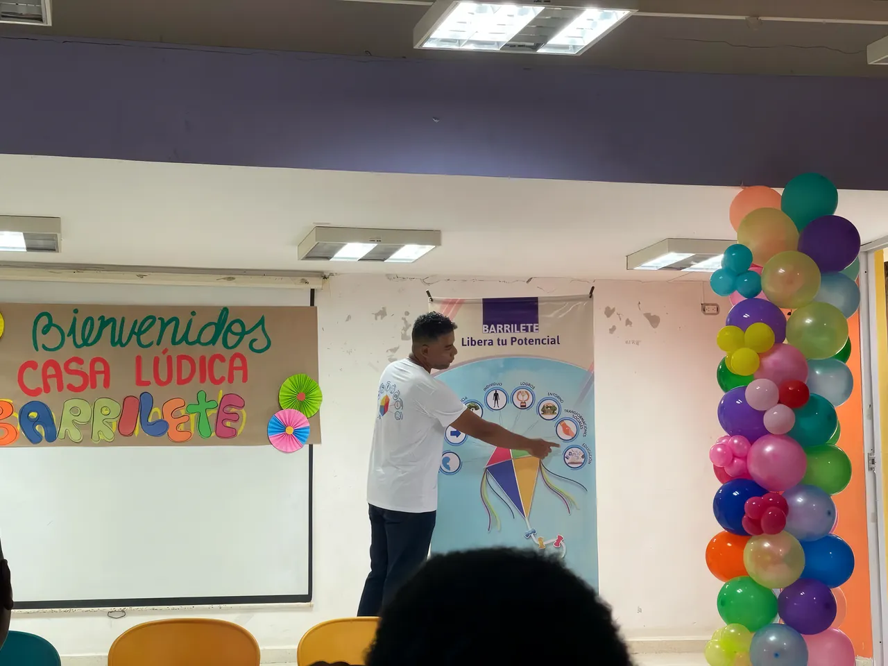 Un facilitador señala el pendón de Barrilete junto al letrero «Bienvenidos Casa Lúdica Barrilete»