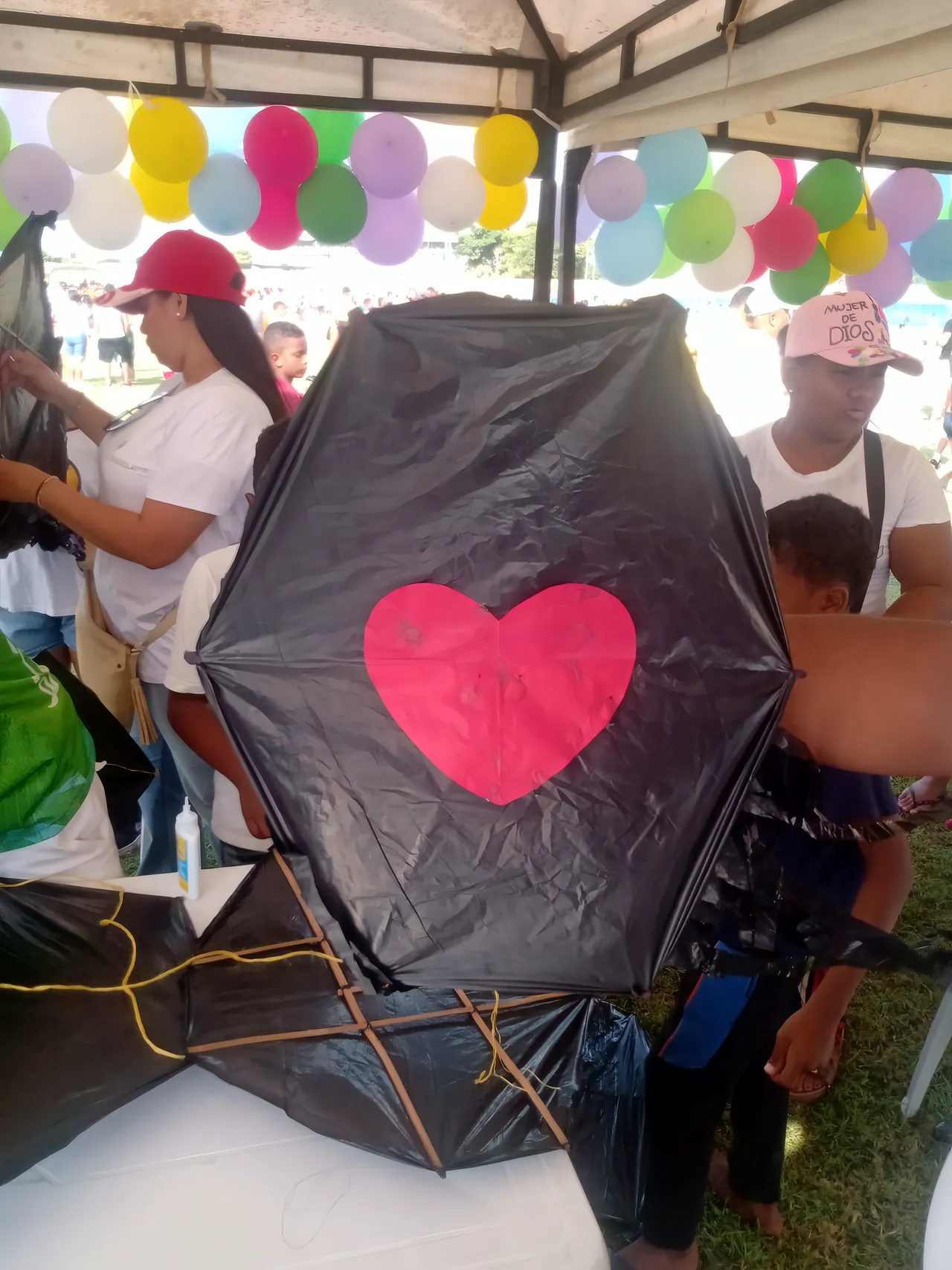 En una feria al aire libre, una participante sostiene un barrilete negro con un corazón rojo