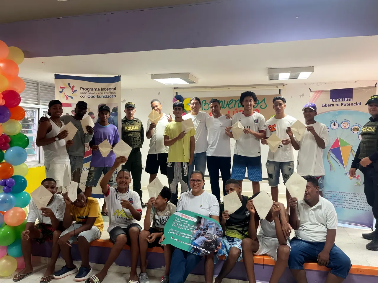 Un grupo grande posa con sus barriletes de papel en un salón decorado con globos