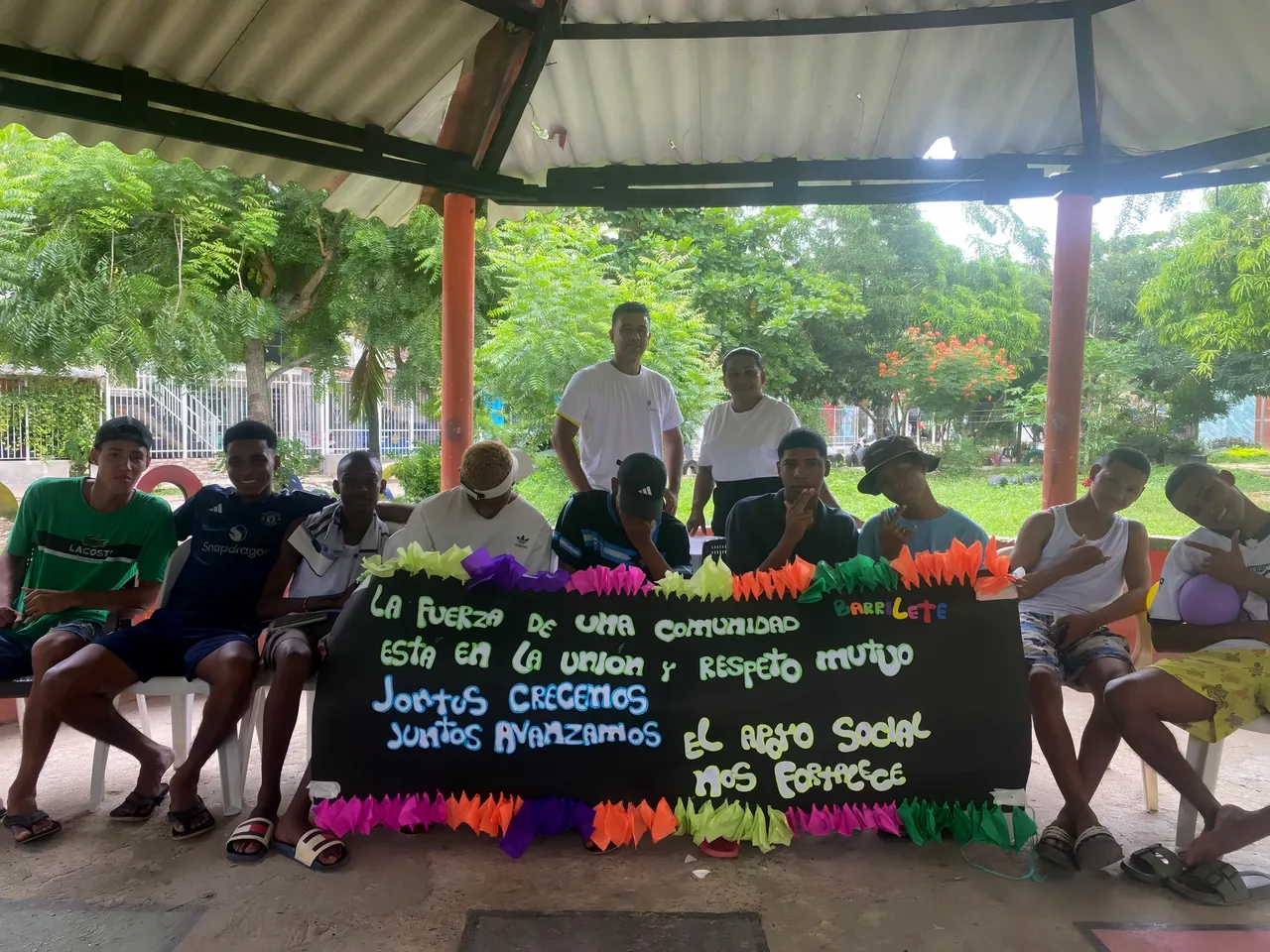 Jóvenes bajo una cubierta sostienen una pancarta: «La fuerza de una comunidad está en la unión y respeto mutuo»