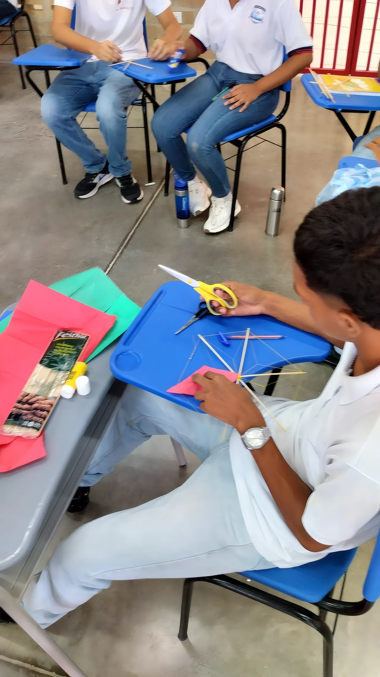 Un estudiante de uniforme recorta papel de colores sobre el pupitre
